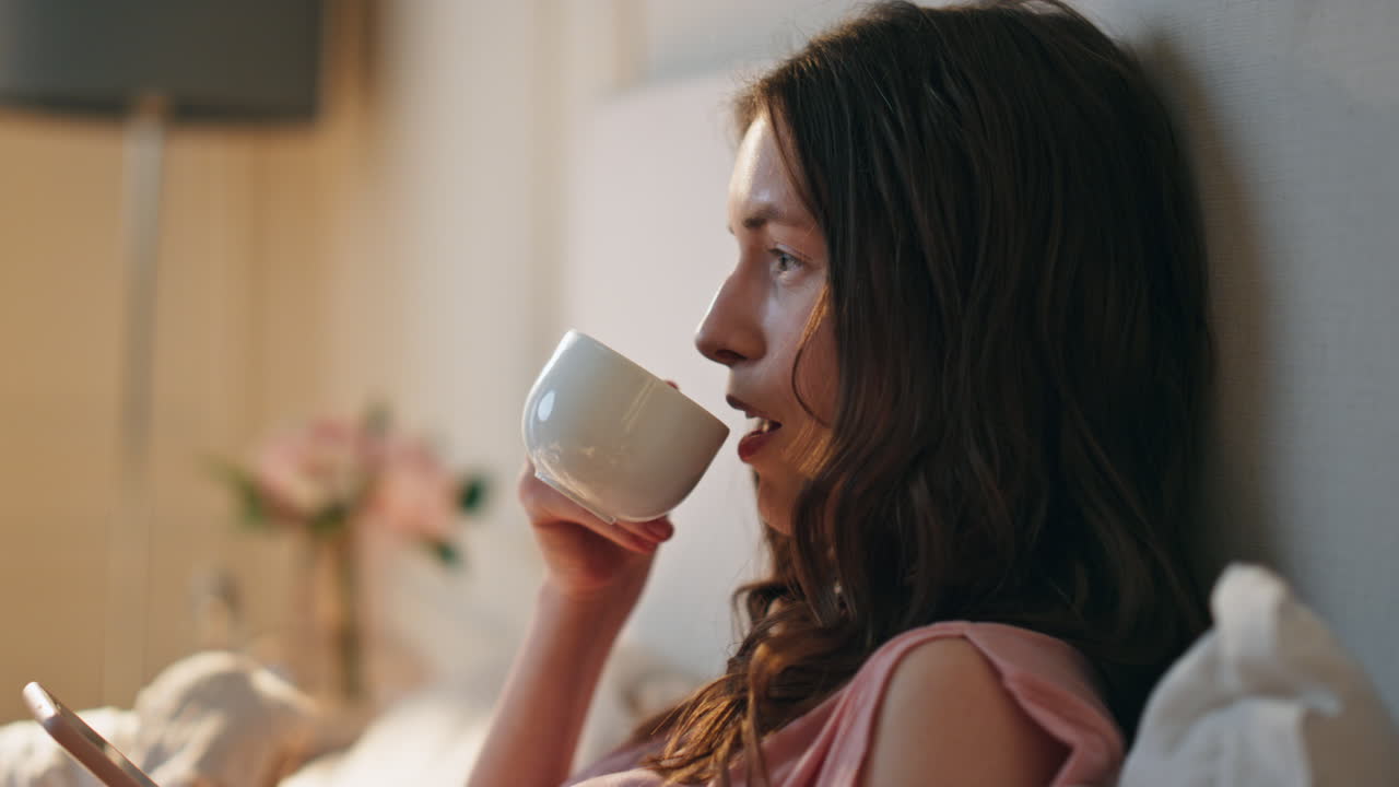 예쁜 소녀를 찾는 스마트 폰 실내 클로즈업. 침착한 여성 술을 마시는 아침