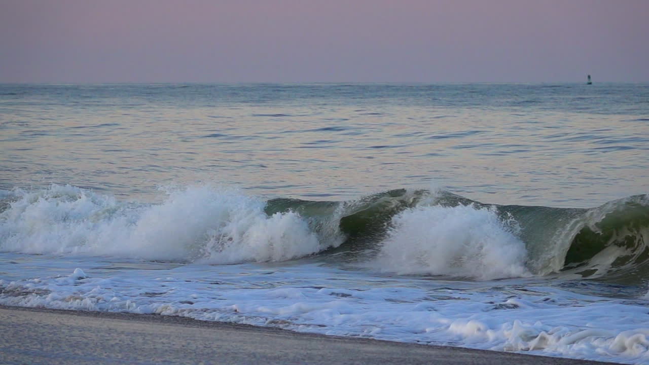 Wave breaks onto shore. Port side buoy in background. Evening light