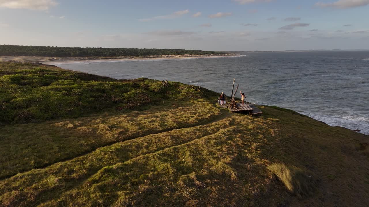 Luftfoto af et par, der står på Cerro Chato-klippen og nyder solnedgangen over Atlanterhavet i Uruguay. Slowmotion