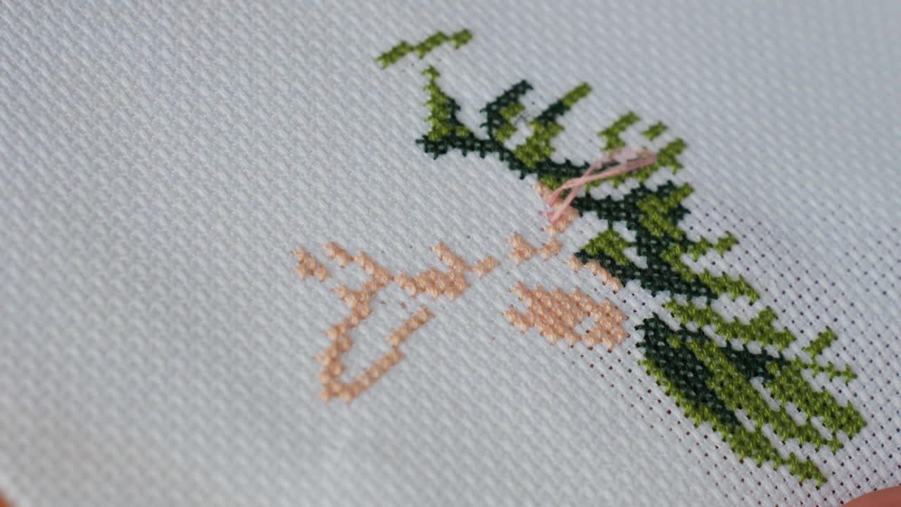 Extreme close up of craft person embroidering green tree on white fabric using pink thread and needle, showing delicate handwork, detailed texture, and precise stitches in calm creative atmosphere