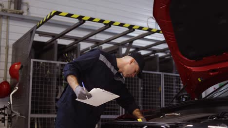 Mechanic-in-a-auto-repair-shot-checking-engine-using-a-tablet,-low-angle