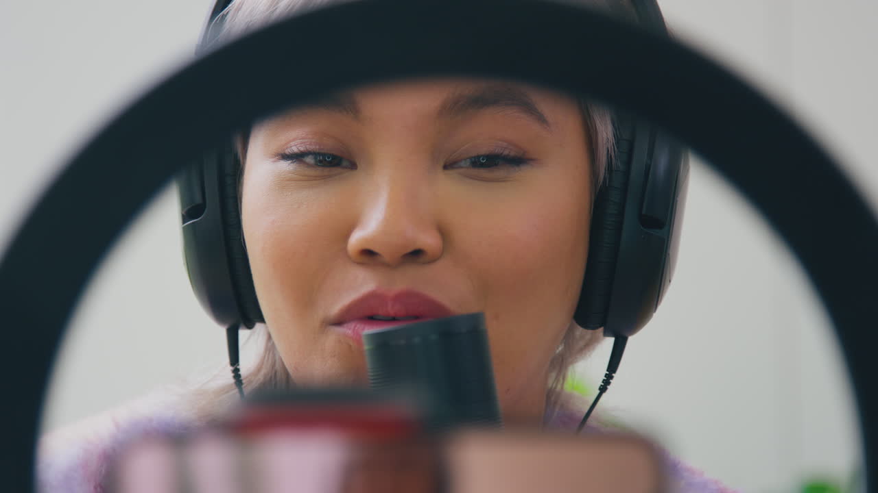 휴대 전화로 라이브 스트리밍을 하는 마이크와 헤드폰을 착용 한 여성 블로거