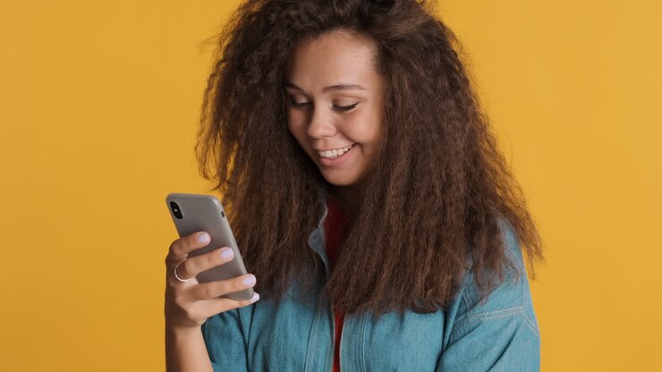 una mujer caucásica de cabello rizado usando un teléfono inteligente y riendo.
