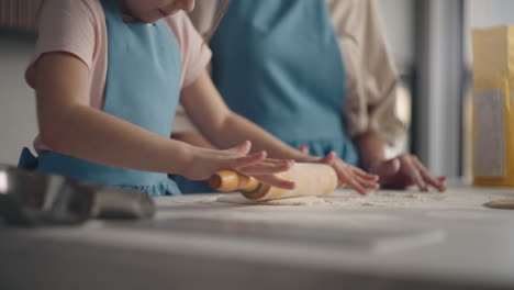 culinary master class for children little girl is rolling out dough for pie or bread in kitchen closeup view