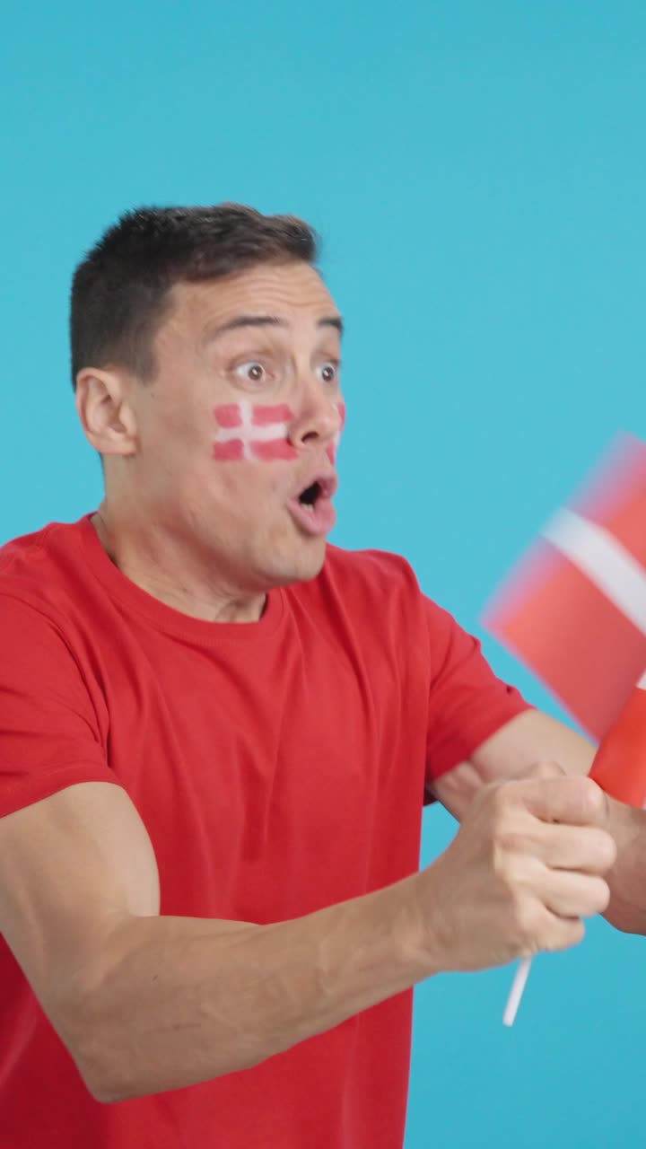 Man cheering for Denmark waving a national flag looking away
