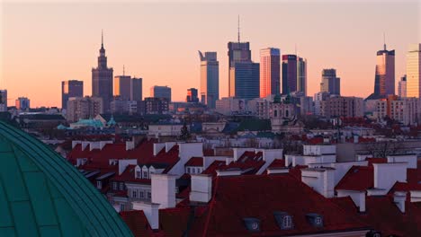 drone pullback with warsaw skyline and st casimir church, palace of culture, and varso tower at sunrise, establishing glow of sunlight in distance
