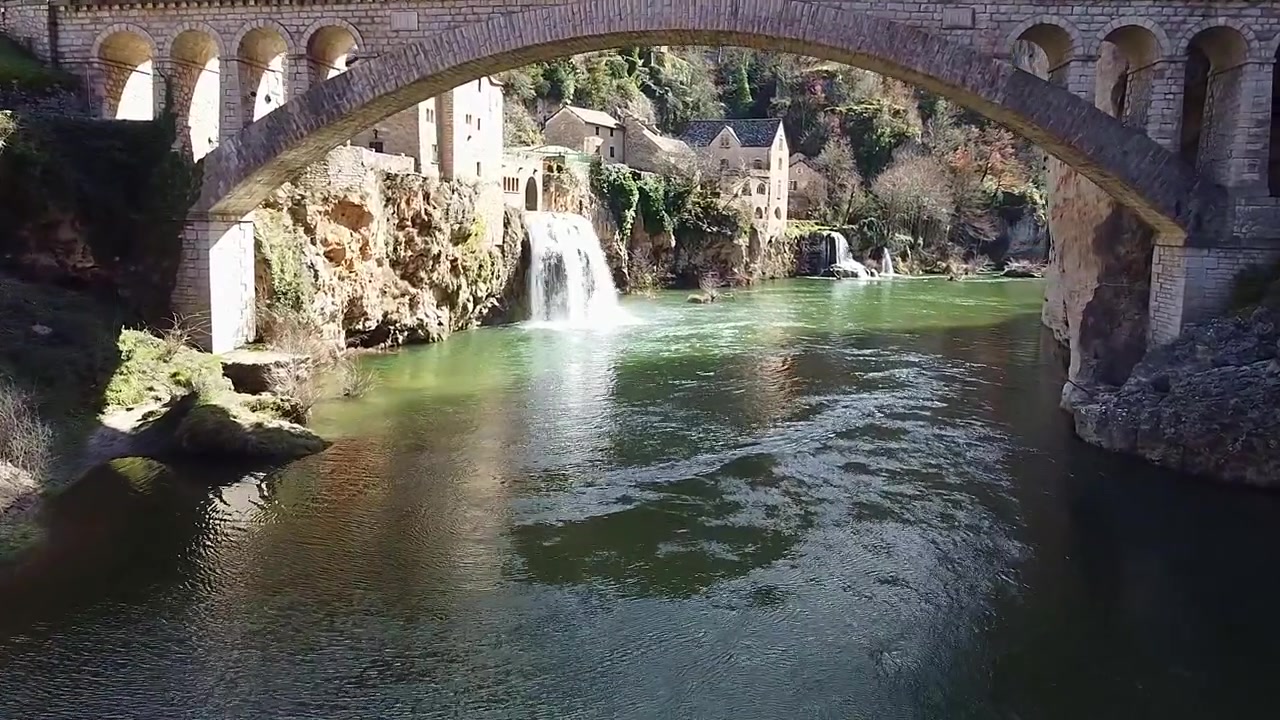 Cascata di Saint-Chély-Du-Tarn. Gole del Tarn. Cascata. Cascata accanto a case in pietra lungo il fiume. Vista aerea ravvicinata. Francia.