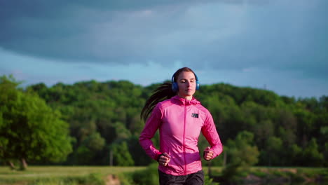 Una-Chica-Con-Una-Chaqueta-Rosa-Y-Pantalones-Negros-Corre-Cerca-Del-Río-Con-Auriculares-Preparándose-Para-El-Maratón