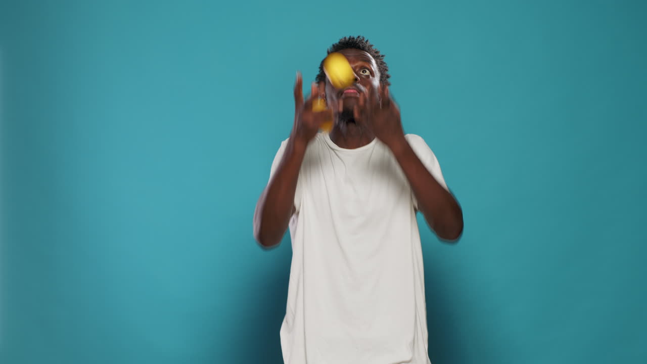 Playful adult juggling lemons and standing over blue background