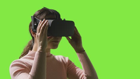 Frau-Setzt-Virtual-Reality-Headset-Auf-Und-Schaut-Sich-Vor-Grünem-Studiohintergrund-Um-1