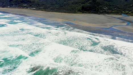 white surfing waves with man windsurfing at piha beach in new zealand