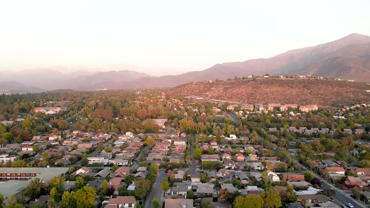 toma de drone de una toma panorámica de las condes en santiago de chile con el cerro apoquindo en el fondo y al atardecer - vista aérea