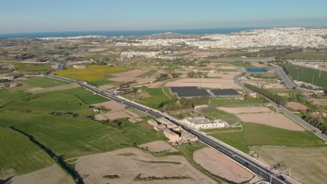 an aerial shot of fields with buildings in the distance and looking out over the sea to the horizon