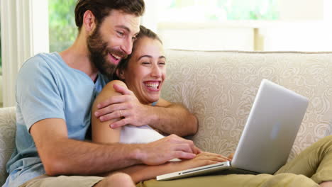 una pareja linda sentada en un sofá con una computadora portátil y abrazándose