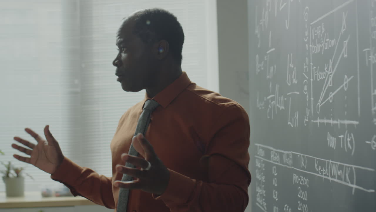 A male professor lecturing and explaining concepts on a blackboard