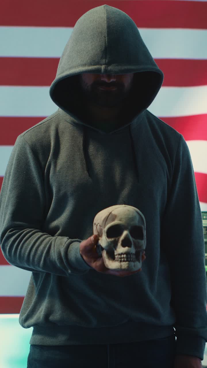 Hacker misterioso con felpa con cappuccio che tiene un teschio sullo sfondo della bandiera americana