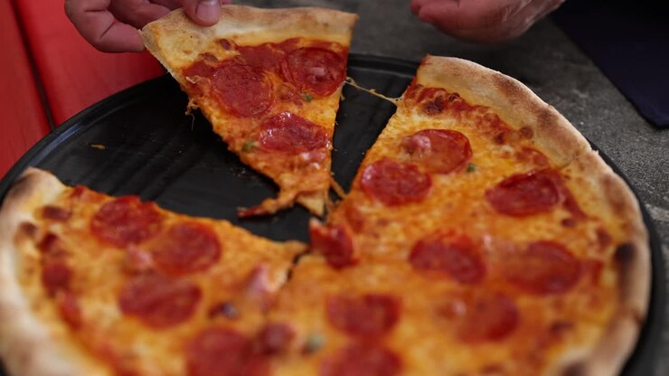 Una mano prende una fetta di pizza al salame piccante da un vassoio, mostrando la sua bontà filante in un ambiente informale