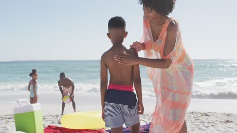 familia afroamericana sonriente usando crema solar en una playa soleada
