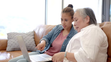 adolescente biracial mostrando el portátil a la abuela asiática en casa