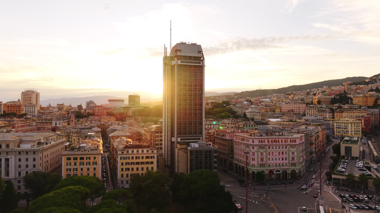 Drone orbiting shot of Genoa, Italy, with a tall modern tower against colorful historic buildings at sunset