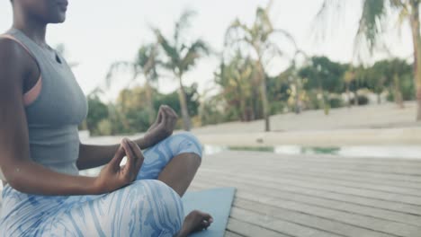 Low-section-of-biracial-woman-practicing-yoga-meditation-sitting-on-jetty,-copy-space,-slow-motion