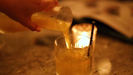 A hand pours a cocktail into a glass in a dimly lit bar, creating a warm, intimate atmosphere