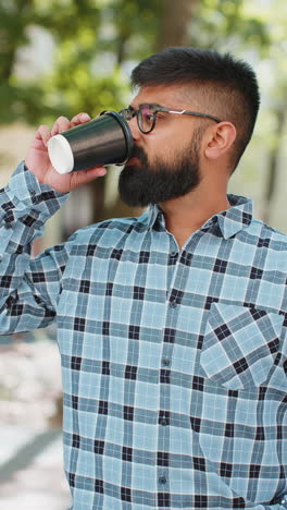 Happy-Indian-man-enjoying-drinking-morning-coffee-hot-drink,-relaxing,-taking-a-break-on-city-street