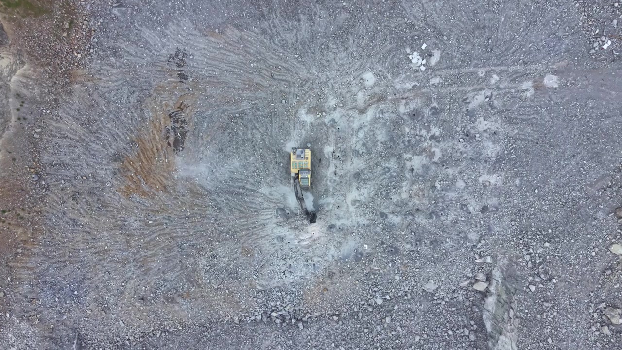 Escavatore al lavoro su un sito ghiaioso in un'area remota durante le ore diurne, concentrato sulla bonifica del terreno e sui lavori di costruzione