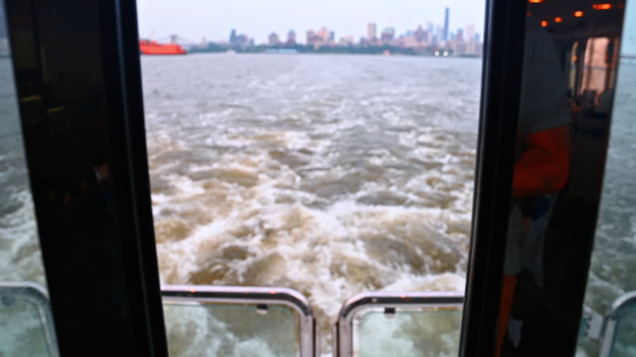 Blick von der Fähre auf die Skyline von New York. Kielwasser hinter der Fähre mit der fernen Skyline von New York City auf der anderen Seite des Wassers
