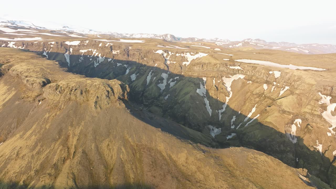 아이슬란드 의 클루푸르르길 협곡 의 드론 촬영, 은 하늘 아래 의 거친 절벽, 초록색 고지대, 눈 인 산 들