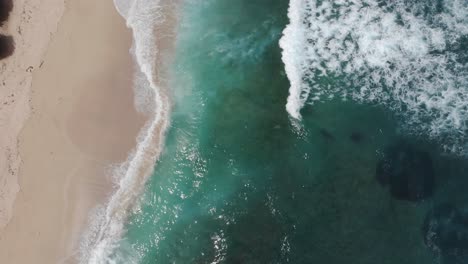 top down aerial view of tropical beach with azure blue, turquoise water and foaming ocean waves crashing on wild beach