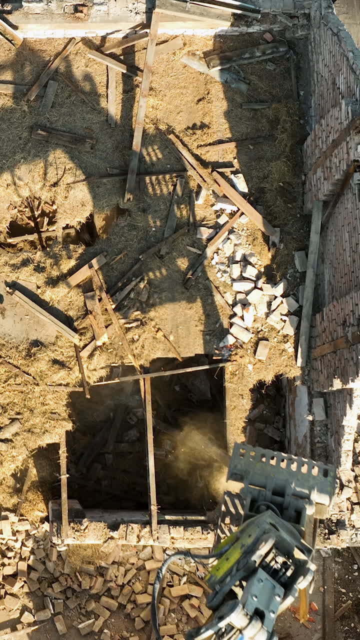 Un'inquadratura cinematografica dall'alto che mostra il braccio di un escavatore che demolisce una casa di mattoni abbandonata. Utile per progetti di costruzione, riqualificazione urbana e sostenibilità