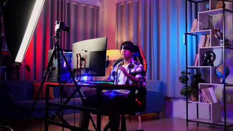 asian boy streamer playing game, touching, and swiping experience virtual reality in futuristic goggles. player touching air panel. personal computer on desk illuminated by rgb led strip light