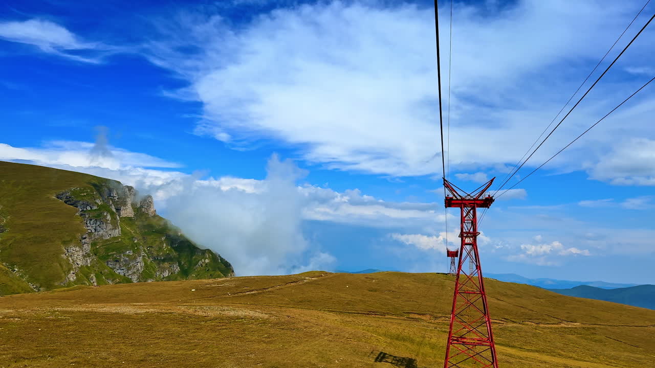 Moving by the cable way by the high mountain. Beautiful azure sky with white clouds at backdrop. The Bucegi Mountains of the Southern Carpathians, Romania