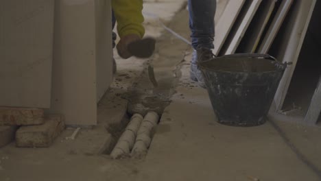 construction worker spreads cement over pipes with trowel