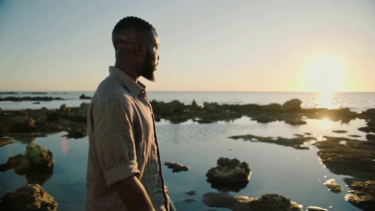 Placing laptop, man with rolled sleeves and wristwatch walking shore, watching sunset, copy space