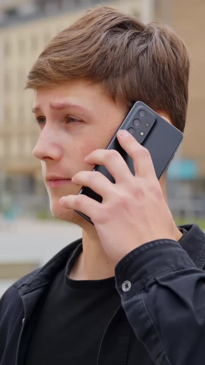 Young man talking on phone outdoors, urban background, casual mood, vertical