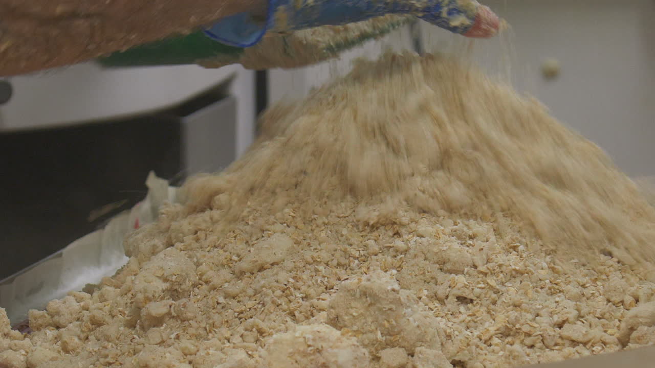 A worker uses a scoop to add the correct mix of topping for a tray of cake slice