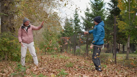 young woman and her nephew joyfully playing outdoors as she sprays dry autumn foliage on them, both laughing and enjoying the moment amidst the natural autumn scenery