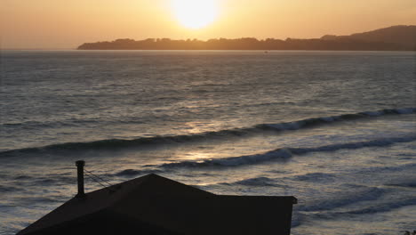 Silueta-De-Una-Cabaña-En-Un-Barranco-Empinado-Con-El-Océano-Y-La-Puesta-De-Sol-En-El-Fondo---Lapso-De-Tiempo