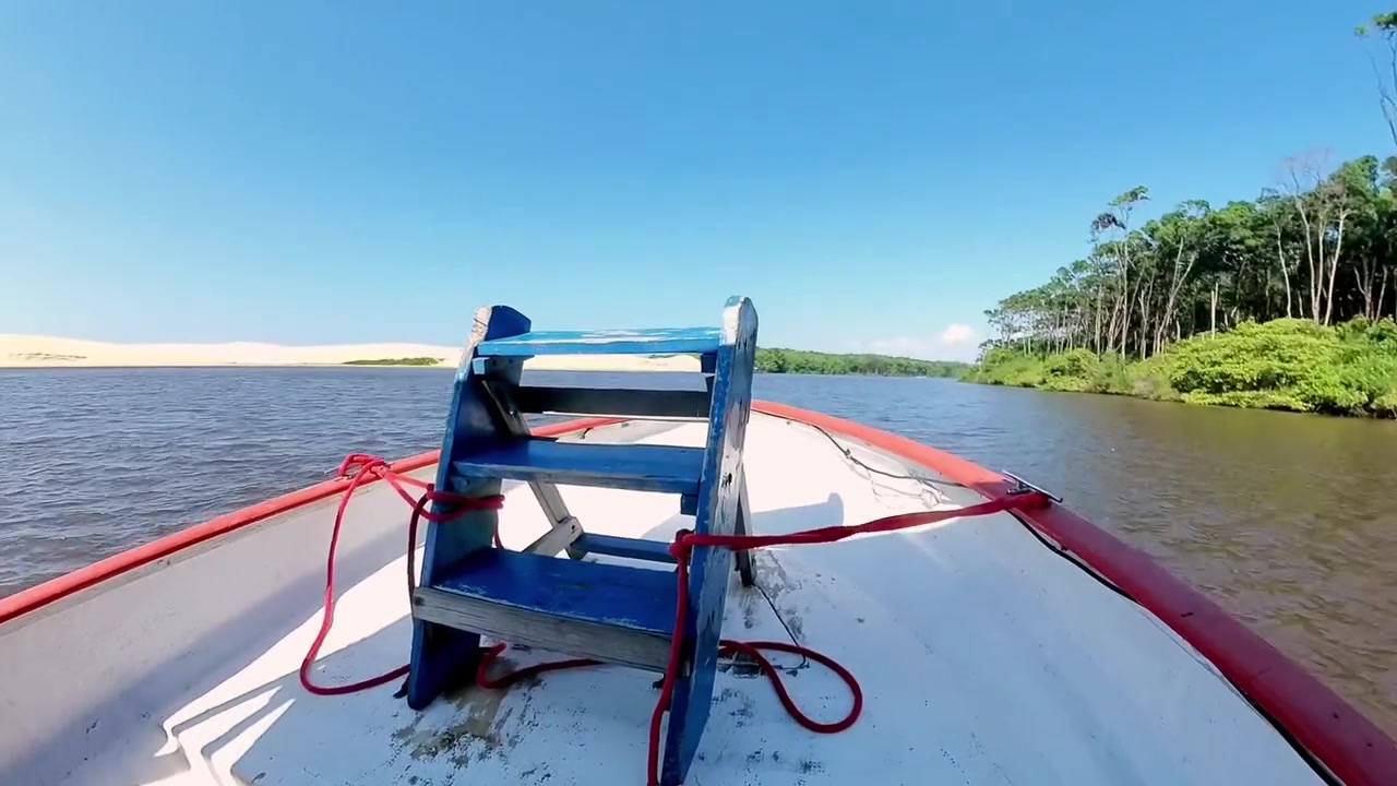 Sideutsikt fra en motorbåt som suser langs Preguiça-elven i Barreirinhas, Brasil, og skaper et skummende hvitt kjølvann mot palmetrær og frodig grønt