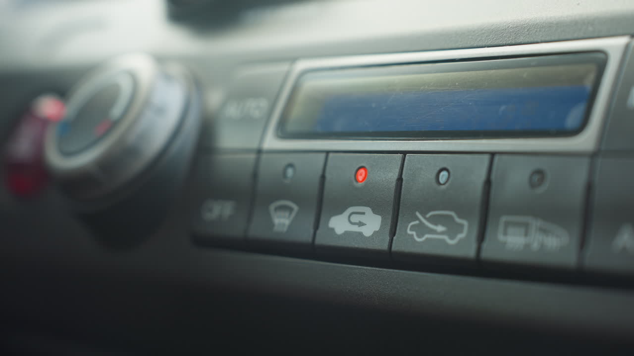close up finger pressing off button on car climate control panel to disable ac while illuminated recirculation and vent icons glow under soft daylight for authentic cabin interior detail