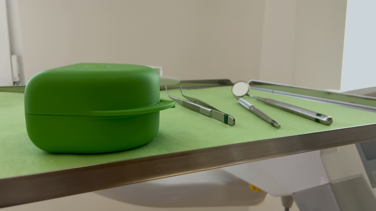 las herramientas de un ortodoncista o dentista, dispuestas en una bandeja verde, junto a una caja de plástico para aparatos ortopédicos