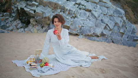 attractive girl enjoying picnic at sandy shore. dreaming lady holding fruits