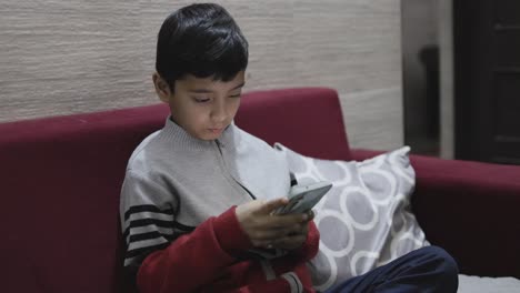 young kid watching mobile and playing online game at home at night from different perspective