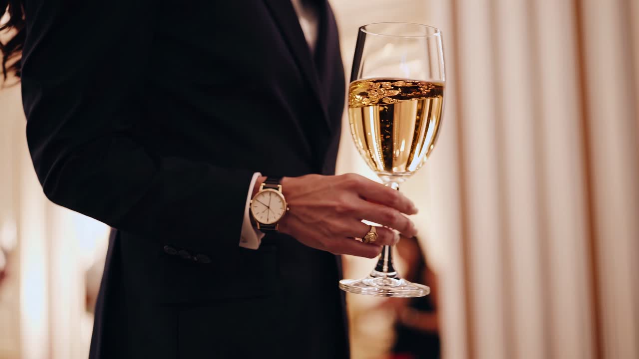 Elegante primo piano di una persona in abito formale che tiene in mano un calice di vino, ripresa da un angolo laterale