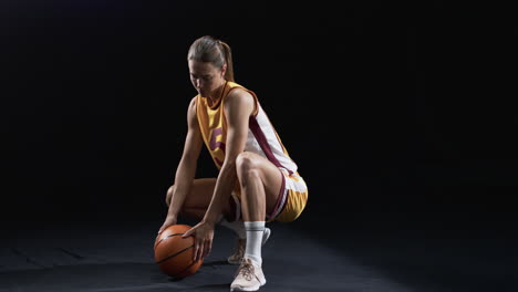 young caucasian woman poses in basketball attire on a black background