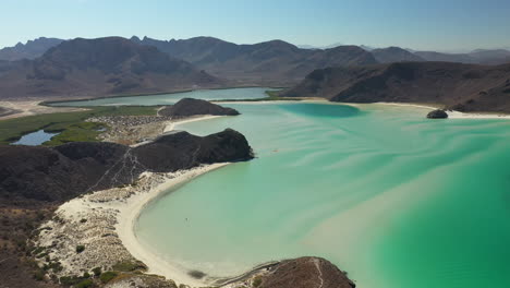 cinematic tilting upward drone shot of balandra beach, view of red hills, turquoise waters, white-sand beaches, and mountains