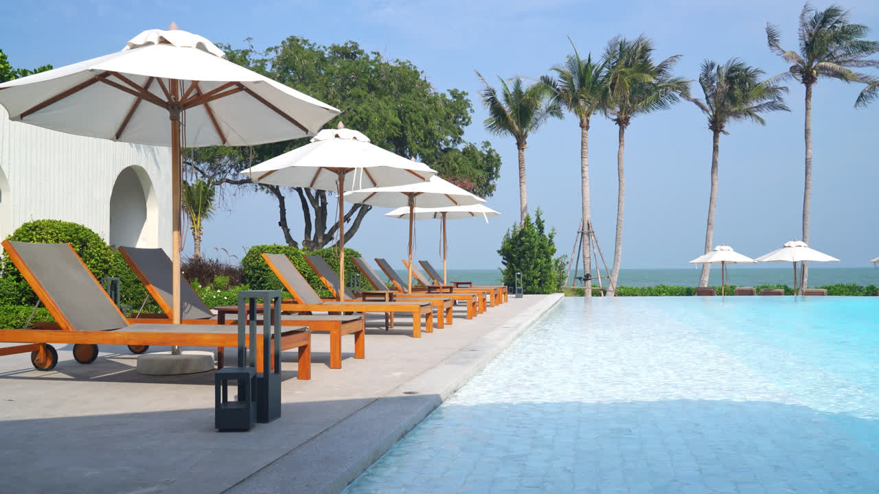 바다를 배경으로 수영장 주변에 침대 수영장이 있는 우산 - 휴일 및 휴가 개념