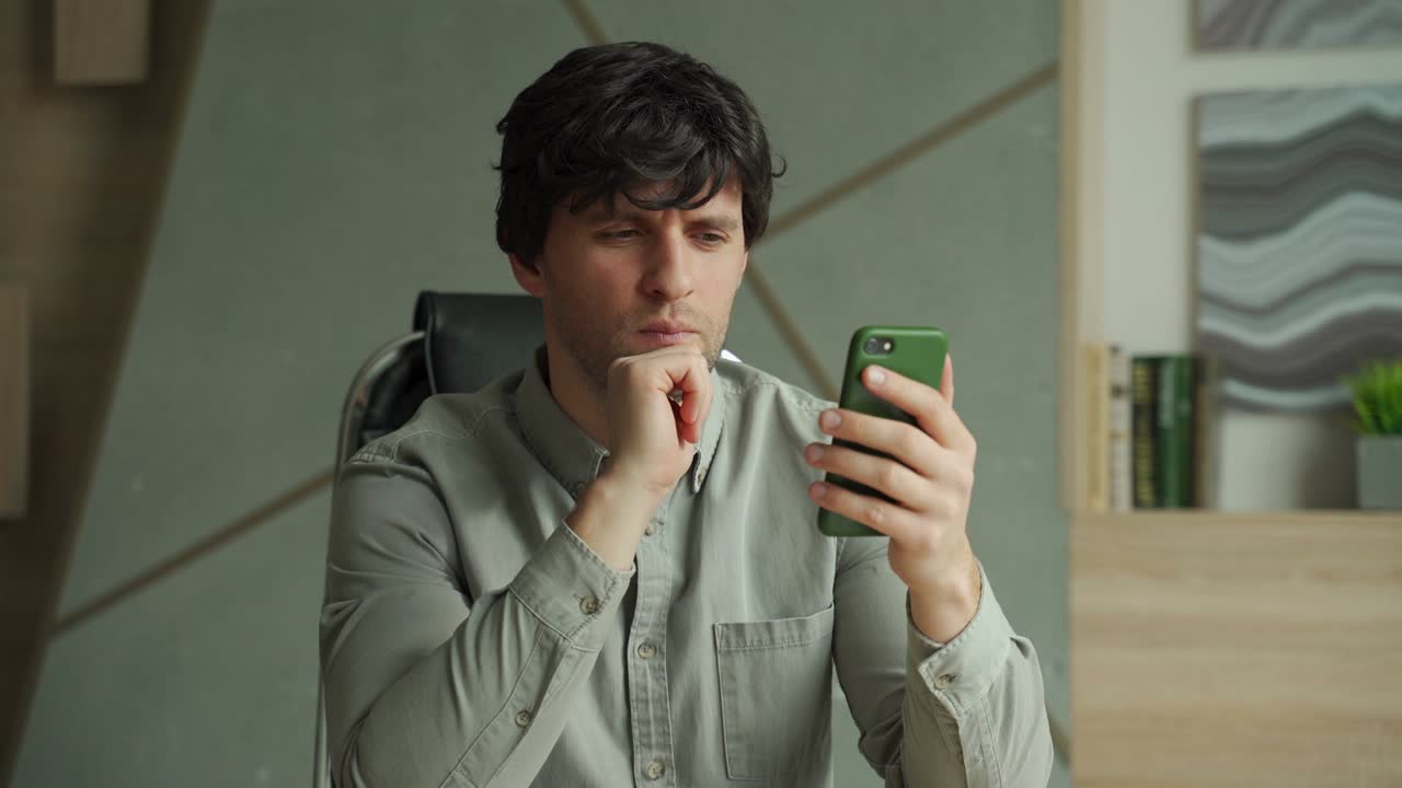 Brooding young man working in a modern studio-office. A person using a smartphone